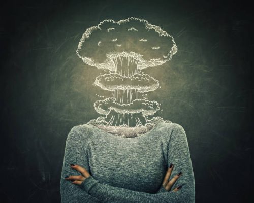 Surreal image young woman head explosion over blackboard background. Mental state of human with lot of problems. Nervous person with crossed hands and a nuclear mushroom sketch, business failure.
